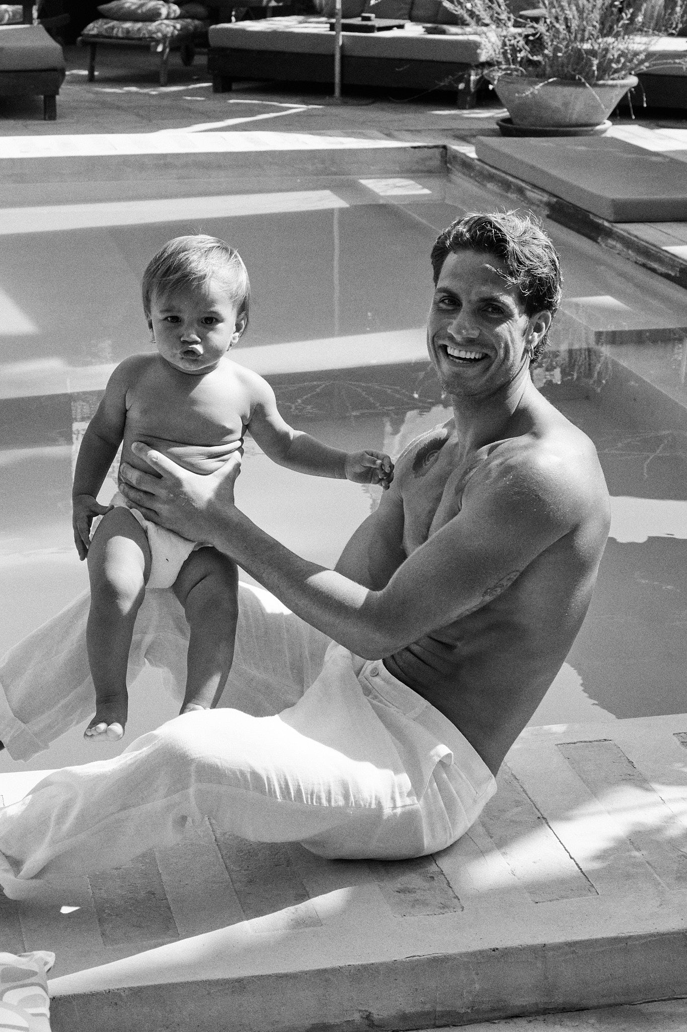 Dad holding a baby in a Rebelalike diaper by the pool, black and white