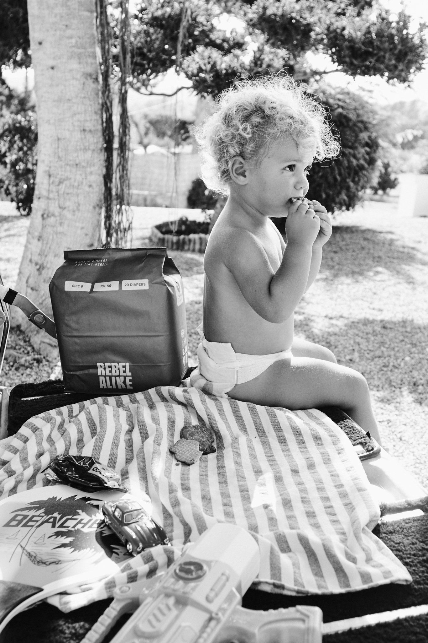Toddler in a Rebelalike diaper with a pack of Rebelalike diapers under a tree, black and white