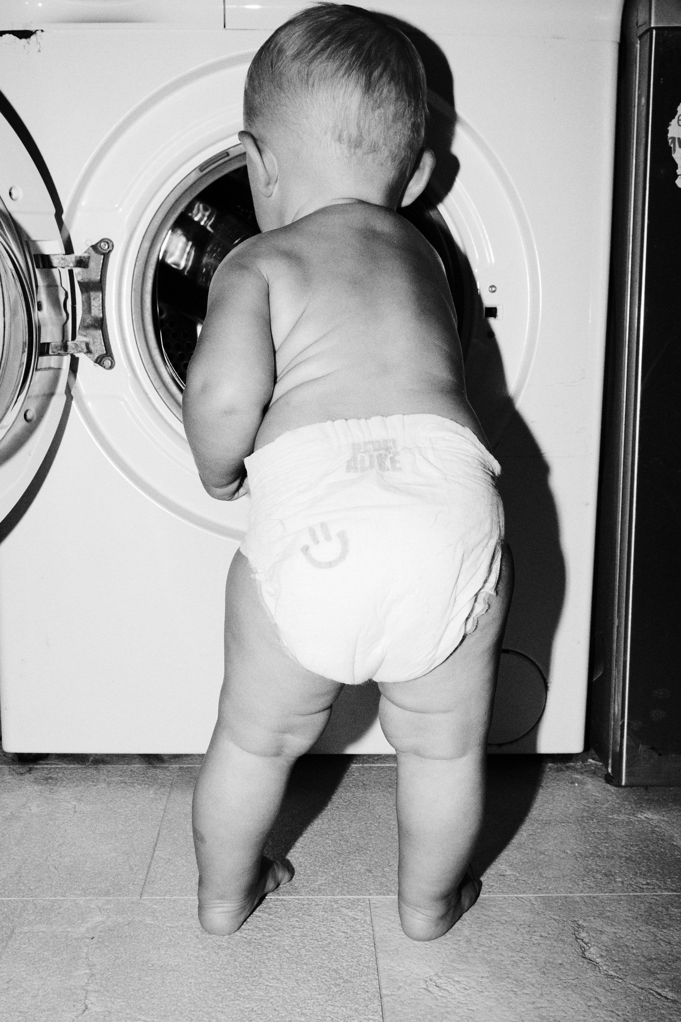 Toddler in a Rebelalike diaper looking into a washing machine, black and white