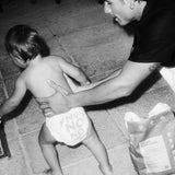 Toddler in a Rebelalike diaper walking past a pack of Rebelalike diapers, black and white