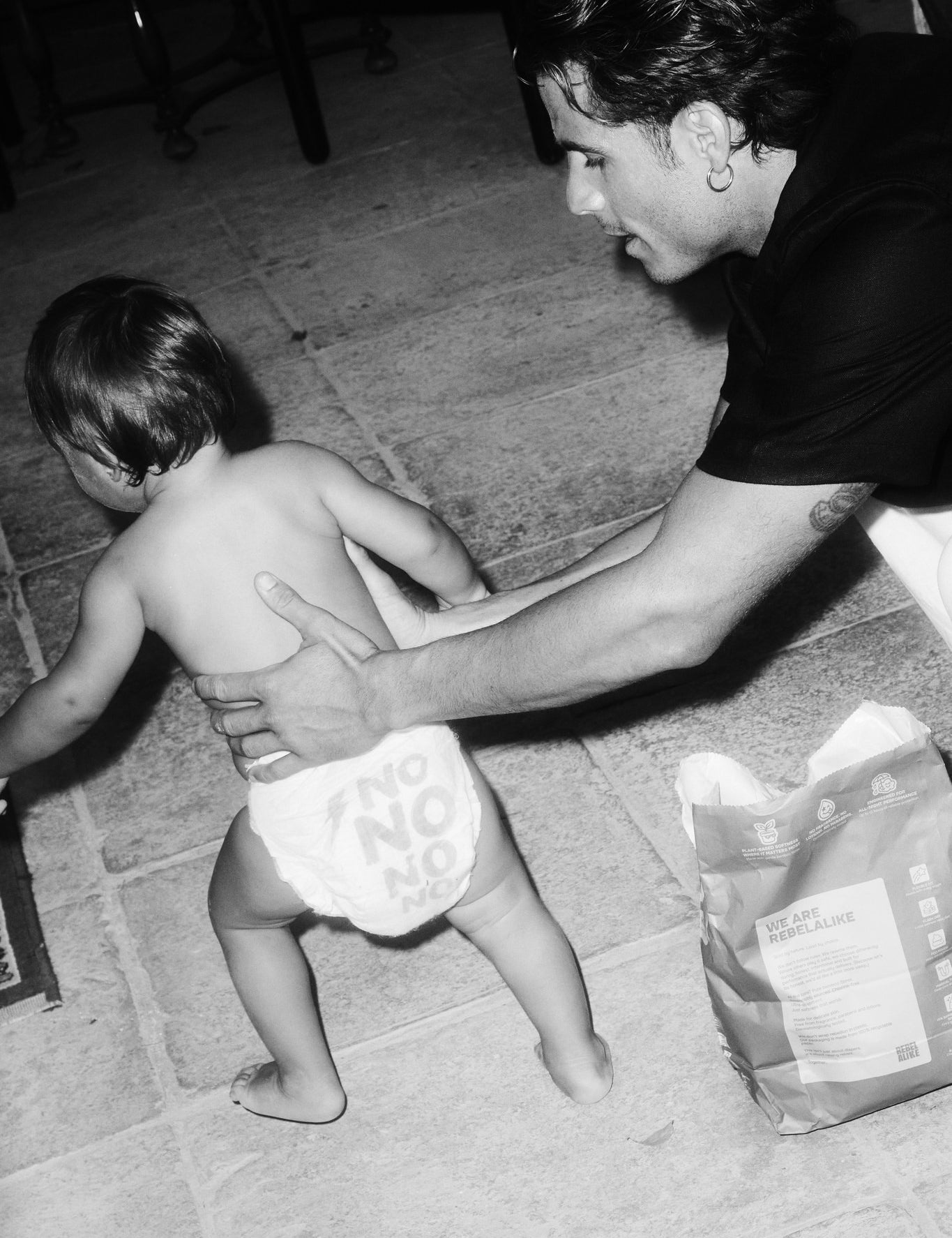 Toddler in a Rebelalike diaper walking past a pack of Rebelalike diapers, black and white