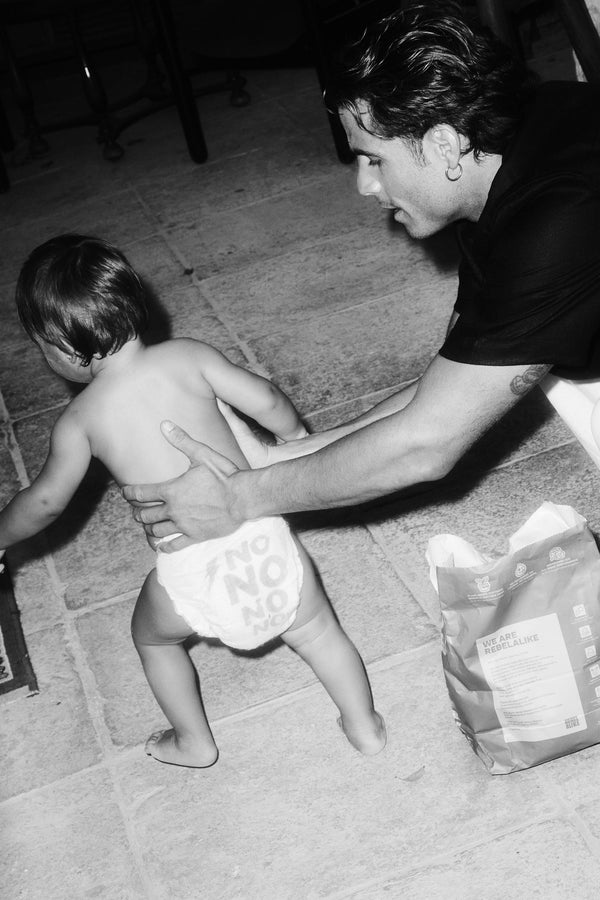 Toddler in a Rebelalike diaper walking past a pack of Rebelalike diapers, black and white
